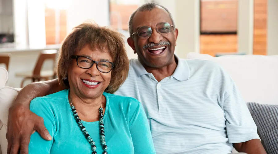 Happy senior couple sitting on a sofa, smiling with confidence after consulting with an Elder Law Lawyer about their estate and future planning.