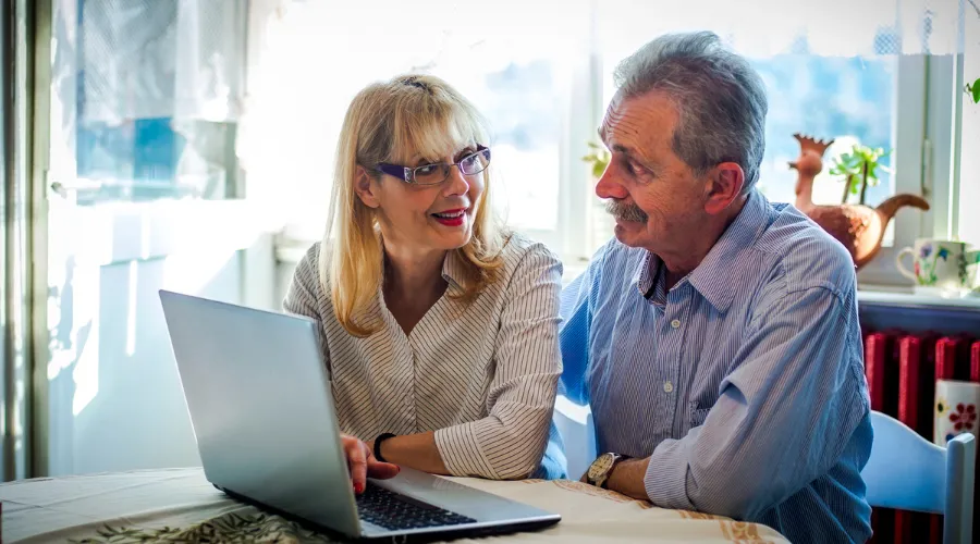 Senior couple sitting at a kitchen table, discussing their future with a laptop in front of them, preparing for estate planning and legal protection with an Elder Law Lawyer