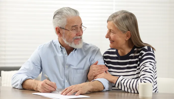 Middle aged couple handing completed paperwork looking reassured, after Amy handels their Medicaid eligibility requirements.